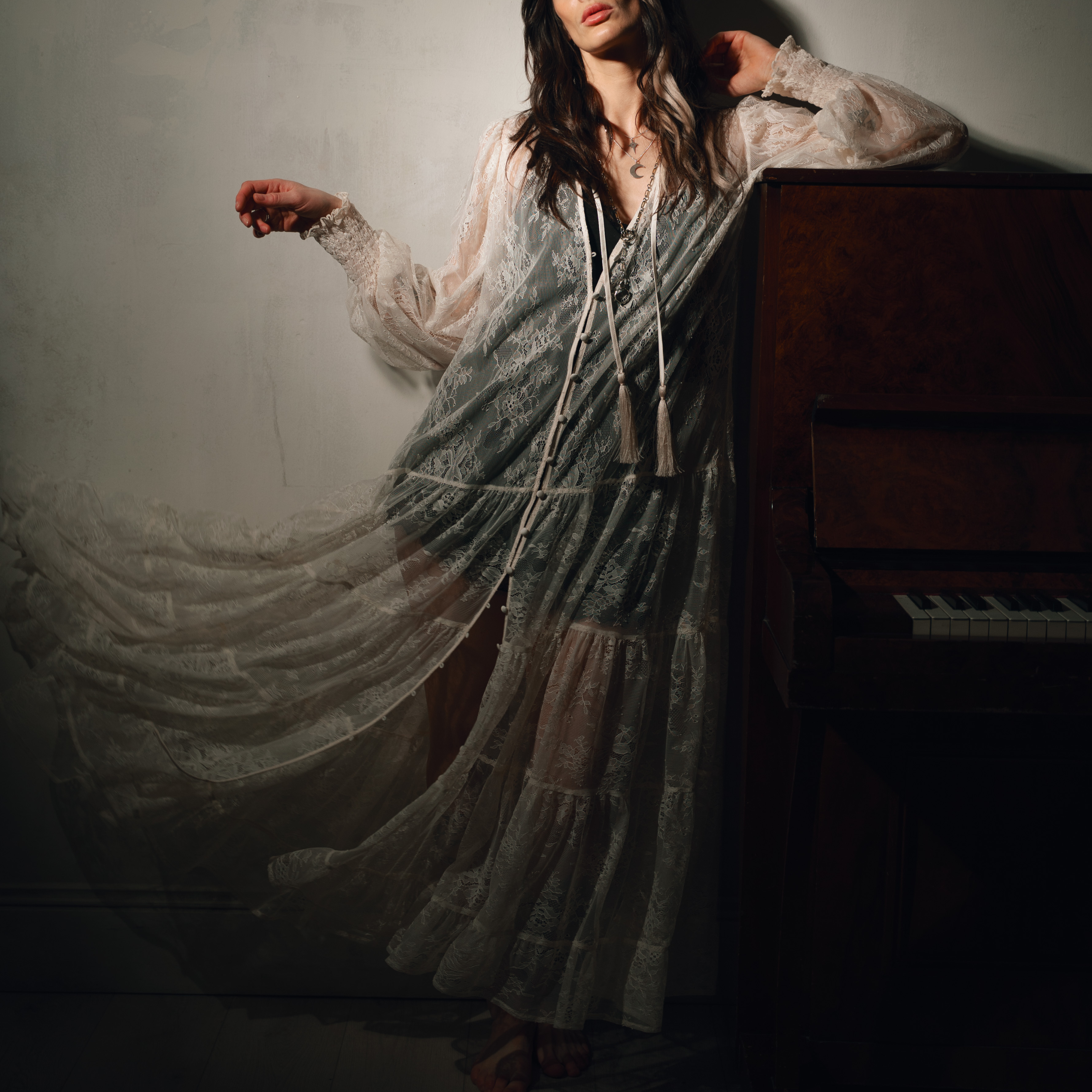 Model Victoria leaning on a piano wearing the Rhiannon Ivory Lace Maxi Dress, a look into the inspiration and making of our first collection of the year, Songbird